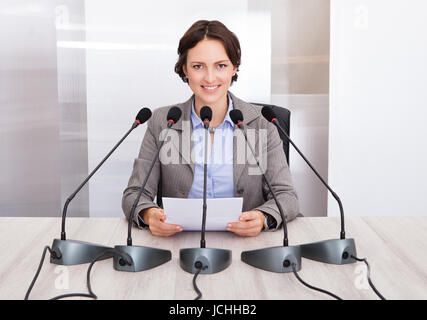 Smiling Businesswoman Holding Paper parlant en face de plusieurs microphones Banque D'Images