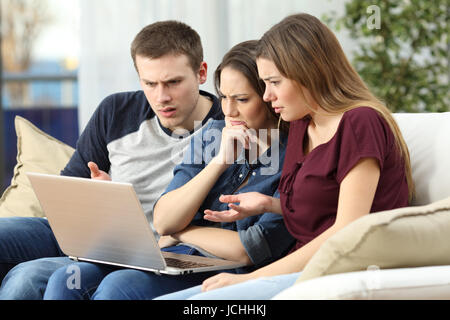 Trois amis en colère en regardant le contenu des médias en ligne en un ordinateur portable assis sur un canapé dans le salon dans une house interior Banque D'Images