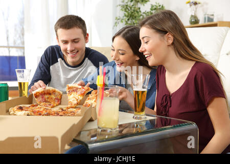 Trois amis parler et manger des pizzas assis sur le plancher de la salle de séjour à la maison Banque D'Images