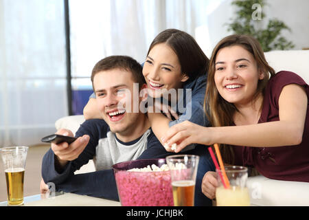 Portrait de trois amis heureux affectueuse watching TV and eating popcorn assis sur un canapé dans la salle de séjour à la maison Banque D'Images