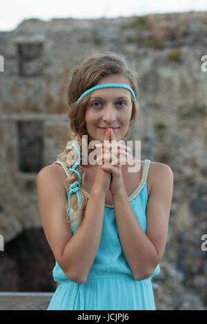 Young blonde woman wearing turquoise haut standing contre mur en pierre médiévale et souriant Banque D'Images