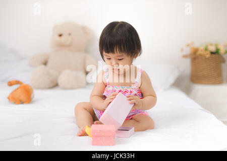 Peu cute asian baby girl sitting on bed jouer Banque D'Images