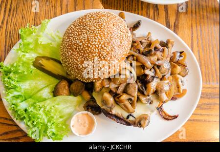 Un plat avec un hamburger avec des champignons sautés sur le dessus, le sésame pain bun, letuce et mayonnaise. Un délicieux hamburger grillé, une malbouffe repas. Banque D'Images