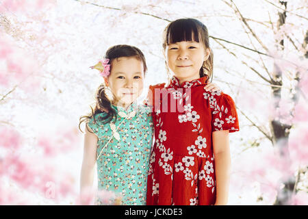 Portrait de deux adorables petits sœurs asiatiques avec abstract blured cerisiers ou sakura fleur arbre contexte . Le printemps. Banque D'Images