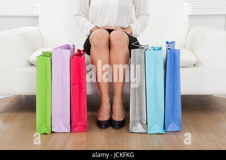 La section basse de businesswoman sitting on sofa avec des sacs multicolores sur le plancher à la maison Banque D'Images