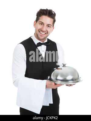 Portrait of smiling waiter holding tray dôme isolé sur fond blanc Banque D'Images