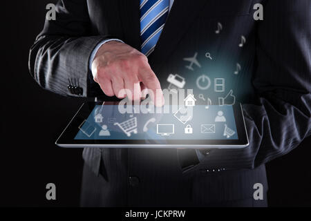 Portrait of businessman using digital tablet avec différentes icônes sur fond noir Banque D'Images