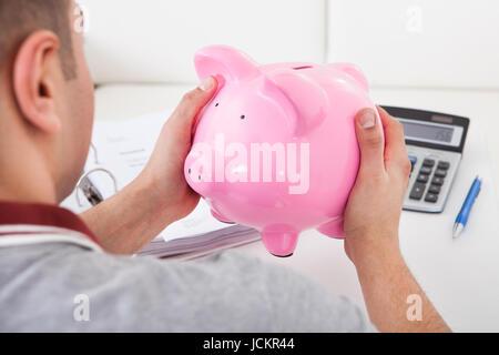 Portrait of young man holding piggy bank à la maison Banque D'Images