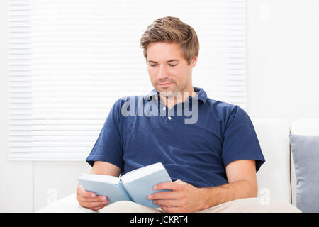 Mid adult man reading book while sitting on sofa at home Banque D'Images