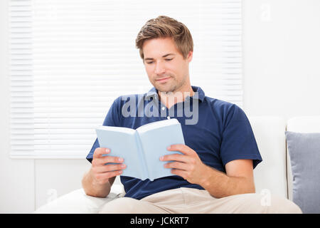 Mid adult man reading book while sitting on sofa at home Banque D'Images
