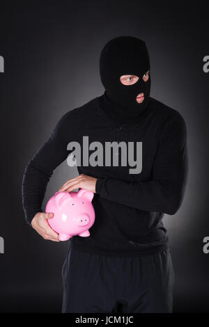 Voleur ou furtif voleur vêtu d'un costume noir et son passe-montagne s'échapper par l'obscurité voler a pink piggy bank de vol conceptuel de l'épargne et placements Banque D'Images