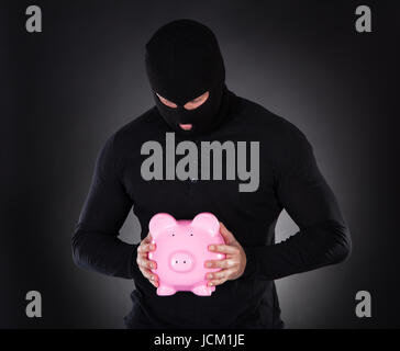 Voleur ou furtif voleur vêtu d'un costume noir et son passe-montagne s'échapper par l'obscurité voler a pink piggy bank de vol conceptuel de l'épargne et placements Banque D'Images