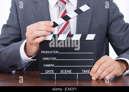 Portrait of businessman holding clapper board at desk Banque D'Images