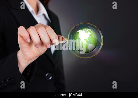 Portrait of businesswoman holding loupe sur globe sur fond noir Banque D'Images