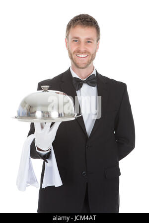 Portrait of smiling waiter holding tray dôme isolé sur fond blanc Banque D'Images