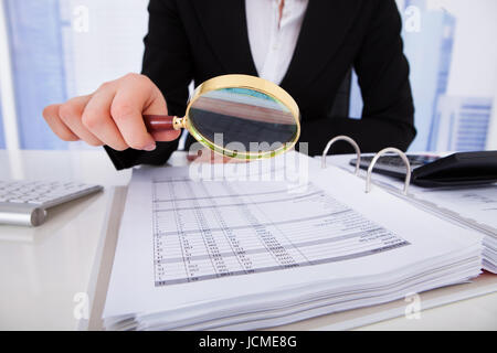 Portrait of young businesswoman de l'examen des factures avec loupe at office desk Banque D'Images