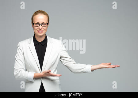 Belle jeune couple tenue blanche et lunettes noires, smiling, holding open palm avec copie vide de l'espace. Femme d'affaires montrant part Banque D'Images