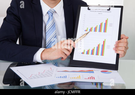 Portrait of businessman showing graphiques at desk in office Banque D'Images