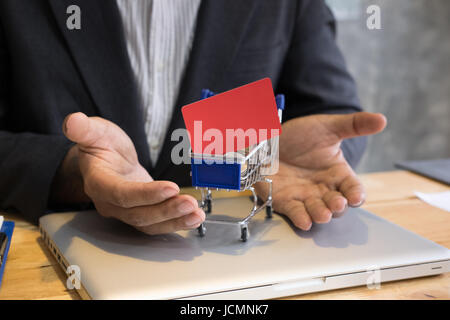 Jeune homme montrant une carte de crédit dans un mini supermarché panier chariot plein de pièces sur un ordinateur portable pour faire des achats en ligne. businessman acheter des biens fro Banque D'Images