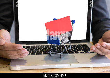 Jeune homme montrant une carte de crédit dans un mini supermarché panier chariot plein de pièces sur un ordinateur portable pour faire des achats en ligne. businessman acheter des biens fro Banque D'Images