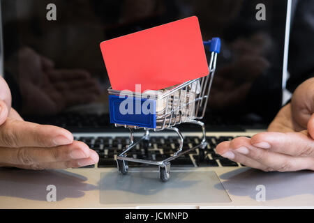 Jeune homme montrant une carte de crédit dans un mini supermarché panier chariot plein de pièces sur un ordinateur portable pour faire des achats en ligne. businessman acheter des biens fro