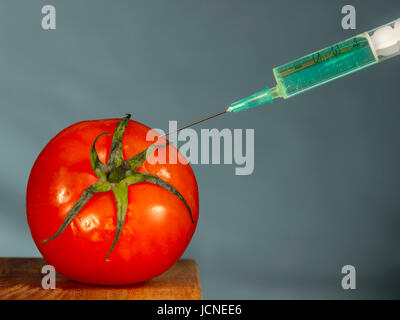 L'injection avec une aiguille hypodermique fond vert vif dans une tomate rouge Banque D'Images