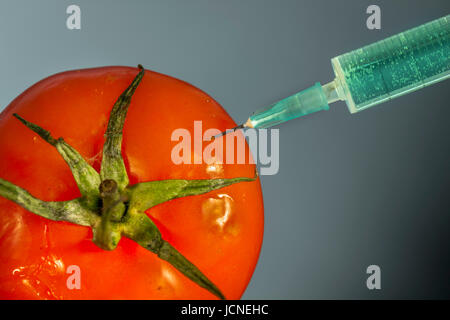 Aiguille hypodermique injectant une substance vert vif dans une tomate rouge Banque D'Images