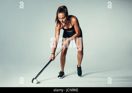 Toute la longueur de balle de hockey balle dribble joueur féminin sur fond gris. Jeune femme hispanique joue au hockey en studio. Banque D'Images