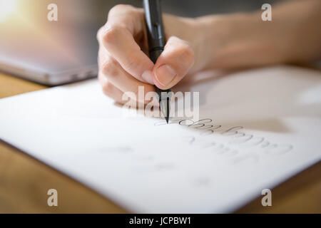 Fermer l'accent sur la main à l'aide d'un stylo noir calligraphie pratique écrit sur du papier blanc avec une lumière douce de coin. Banque D'Images