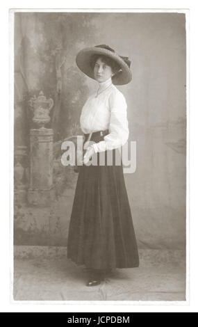 Carte postale, portrait studio de jolie jeune femme édouardienne élégante et glamour portant un grand chapeau à large bord et un chemisier blanc à col haut et une jupe typiques de l'époque, tenant une raquette de tennis, vers 1910, Weymouth, Dorset, Royaume-Uni Banque D'Images