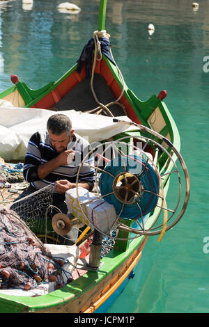 Un pêcheur raccommode ses filets dans ses Luzzu bateau de pêche dans le port de Malte St Julians Bay sur un jour d'été ensoleillé Banque D'Images