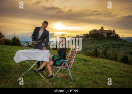 Couple in love boire du vin rouge dans la nature sous les ruines d'un château au coucher du soleil. Banque D'Images