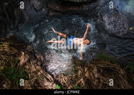 Vue de dessus garçon imbibez le flux depuis le ruisseau qui coule en contrebas de la montagne heureusement, avec la nature des tons sombres Banque D'Images