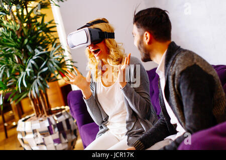 Jeune couple assis dans la salle pendant une jeune femme a lunettes de réalité virtuelle Banque D'Images