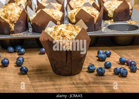 Muffins aux bleuets frais chaud cuit dans les emballages sur une table en bois Banque D'Images