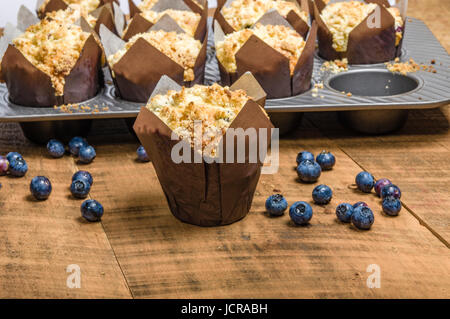 Muffins aux bleuets frais chaud cuit dans les emballages sur une table en bois Banque D'Images