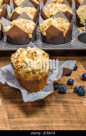 Muffins aux bleuets frais chaud cuit dans les emballages sur une table en bois Banque D'Images