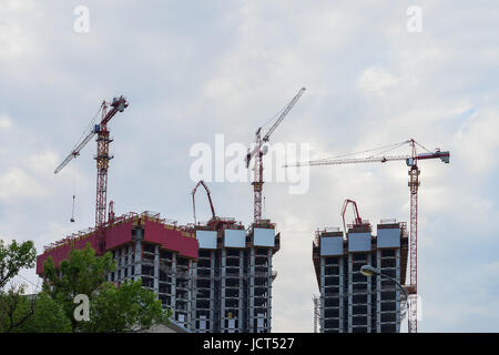 Grues à tour de levage sur site de construction contre l'arrière-plan du ciel bleu, maisons de nouveaux bâtiments à proximité d'une zone résidentielle avec des arbres Banque D'Images