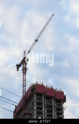 Grue à tour la construction prochaine d'un bâtiment en construction dans le contexte du ciel bleu avec des nuages. La verticale Banque D'Images