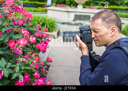 Portrait gros plan du côté jeune homme photographe professionnel pour prendre des photos de fleurs rouges et roses roses avec de l'eau gouttes dans park Banque D'Images