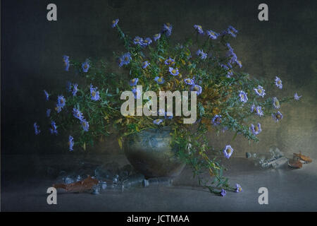 Nature morte avec un grand bouquet d'une petite fleur bleue sur les branches dans un pot en argile et beaucoup de verre transparent petites bouteilles éparpillées sur la table. Banque D'Images