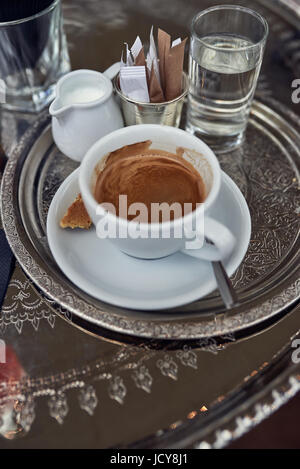 Tasse de café très fort façon expresso avec du lait sur le côté dans une cruche et un verre d'eau sur un plateau dans un restaurant vue close up high angle Banque D'Images