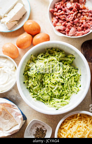 Frittata aux courgettes gâteau () ingrédients mélangés dans un bol blanc - les oeufs, la farine, la courgette râpée, bacon, feta, mascarpone et au cheddar Banque D'Images