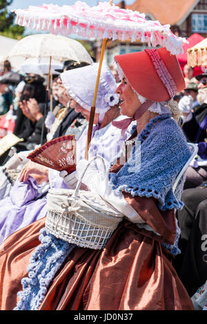 Rangée d'histoire, les femmes âgées, vêtus de costumes colorés victorien classe supérieure assis au soleil, certains fans de portefeuille et des parasols. Banque D'Images