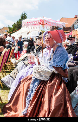 Rangée d'histoire, les femmes âgées, vêtus de costumes colorés victorien classe supérieure assis au soleil, certains fans de portefeuille et des parasols. Banque D'Images