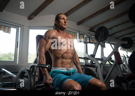 Beau culturiste musculaire faisant poids lourd l'exercice pour le trapezius sur la machine dans la salle de sport Banque D'Images