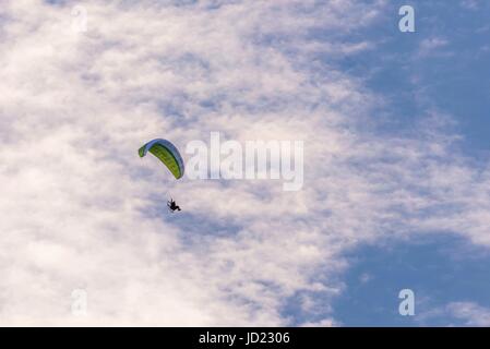 Photo horizontale de seul parapentiste avec vert / blanc ailes et moteur avec grande hélice à l'arrière. Le ciel bleu avec de nombreux nuages est en arrière-plan. P Banque D'Images