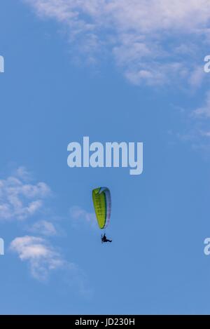 Photo verticale de seul parapentiste avec vert / blanc ailes et moteur avec grande hélice à l'arrière. Le ciel bleu avec quelques nuages est en arrière-plan. Pilo Banque D'Images