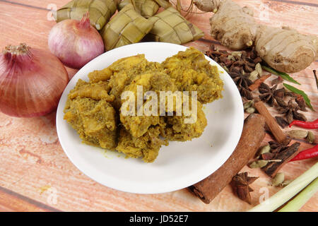 Plat malaisien Rendang Ayam ou poulet au curry sec et Ketupat (NASI) boulette de riz sur fond de bois Banque D'Images