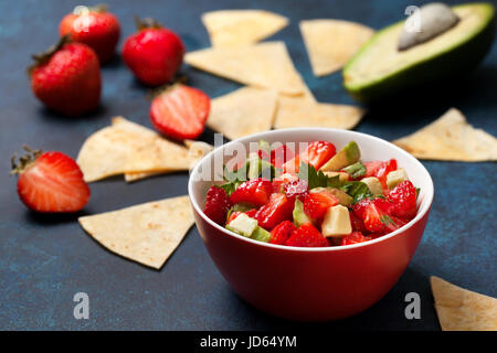 Salsa d'avocat dans un bol de fraises, des fraises fraîches sur fond bleu Banque D'Images